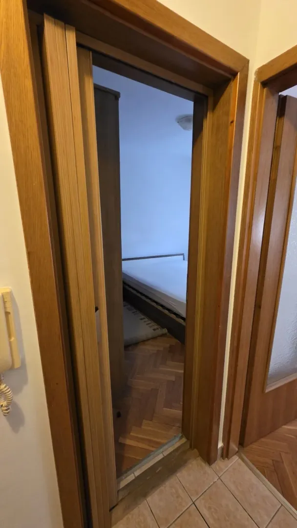 A view through a wooden doorway into a bedroom with parquet flooring.