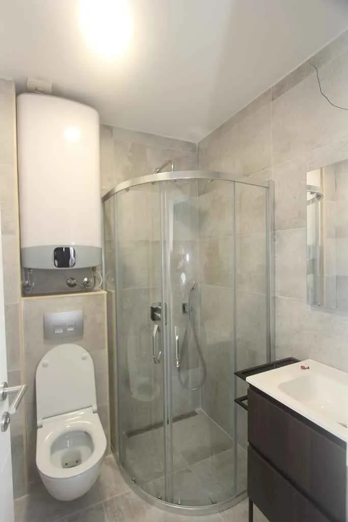 Moderno kupatilo sa tuš kabinom, WC šoljom i bojlerom.
