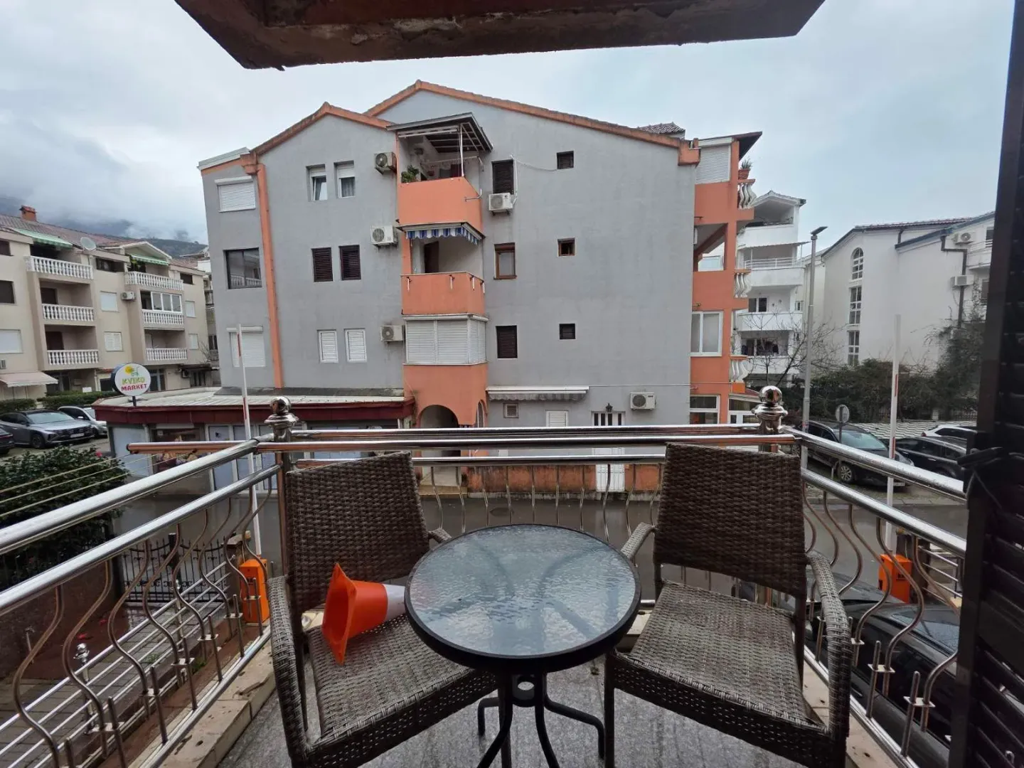 Small furnished balcony with a small table and two chairs, overlooking neighboring buildings.