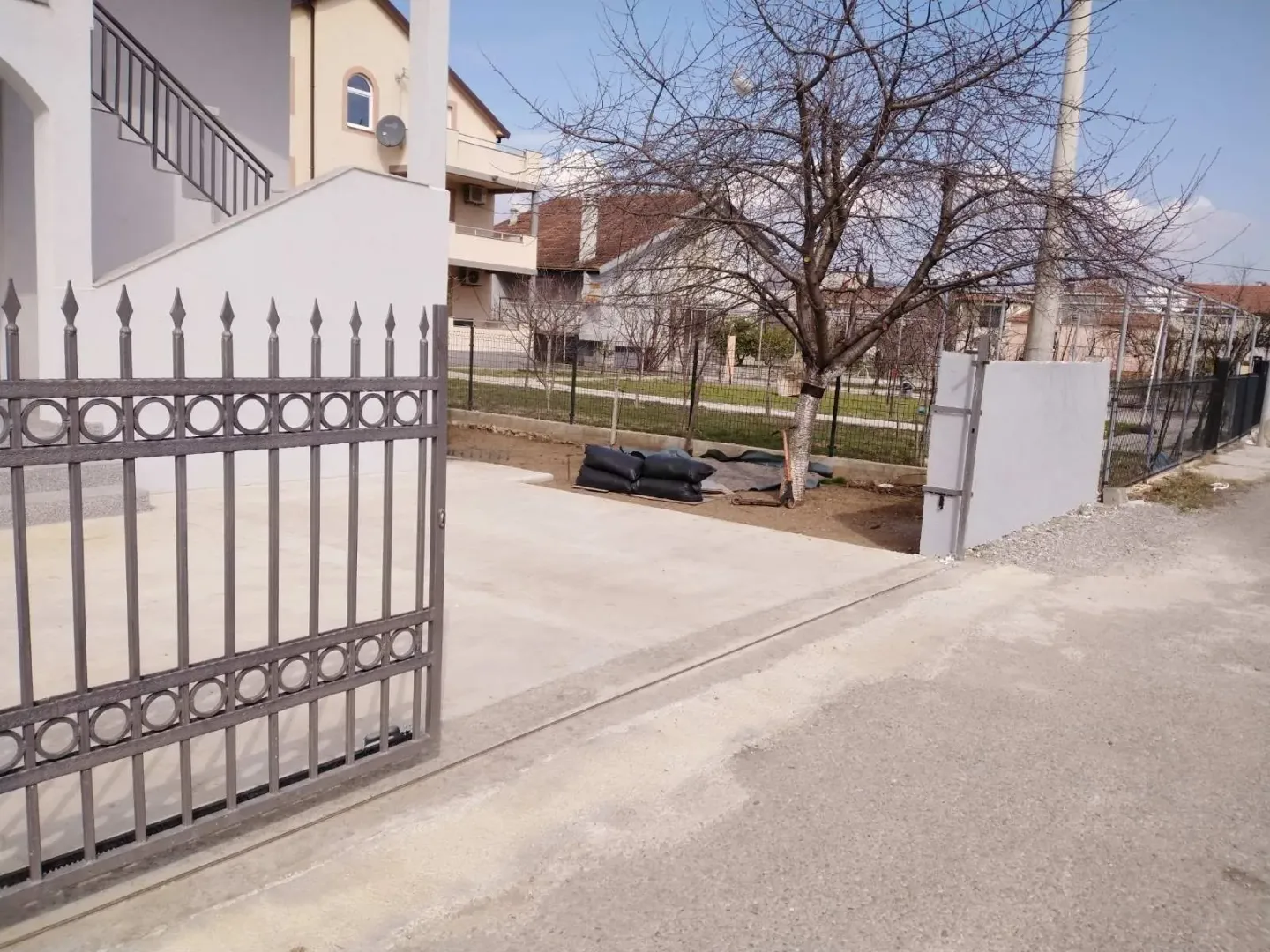 Yard of the house with a metal gate and a concrete driveway.