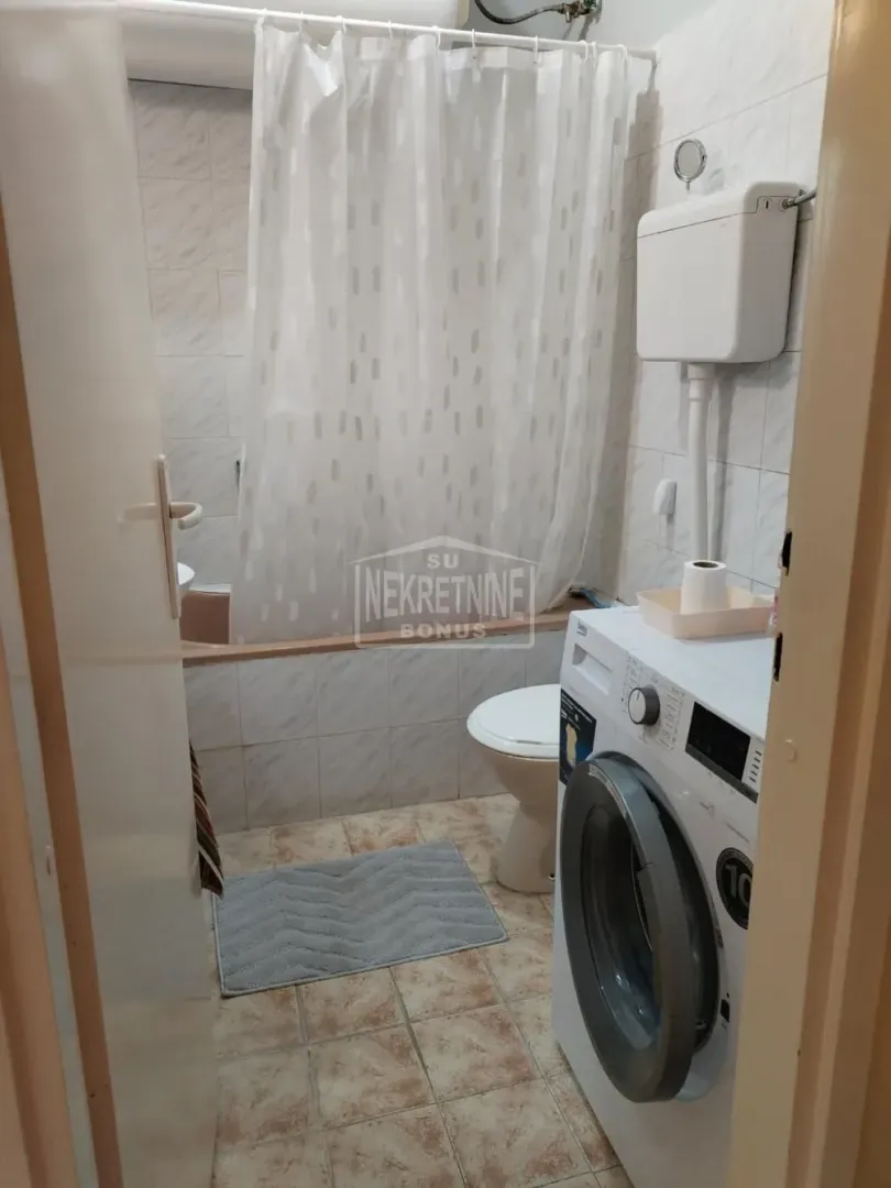 Pogled na kupatilo sa kadom, toaletom i veš mašinom.