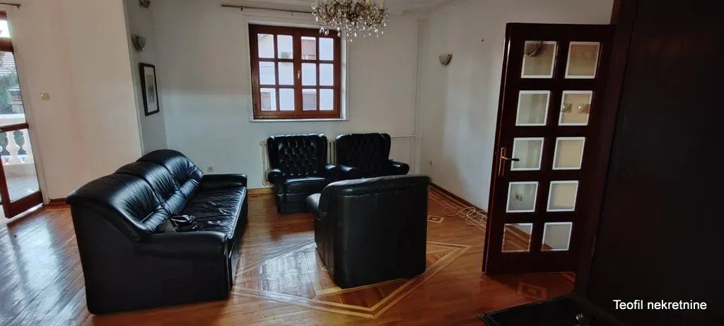 Living room with black leather furniture and wooden flooring.