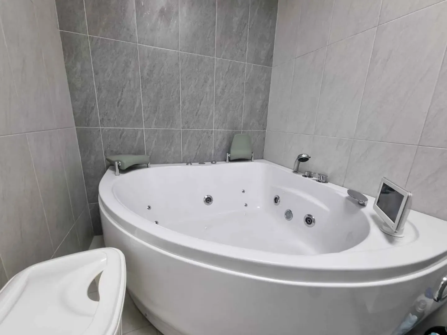Kupatilo sa ugaonom hidromasažnom kadom i sivim pločicama.