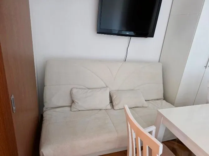 Dnevni boravak sa trosjedom, televizorom na zidu i trpezarijskim stolom.