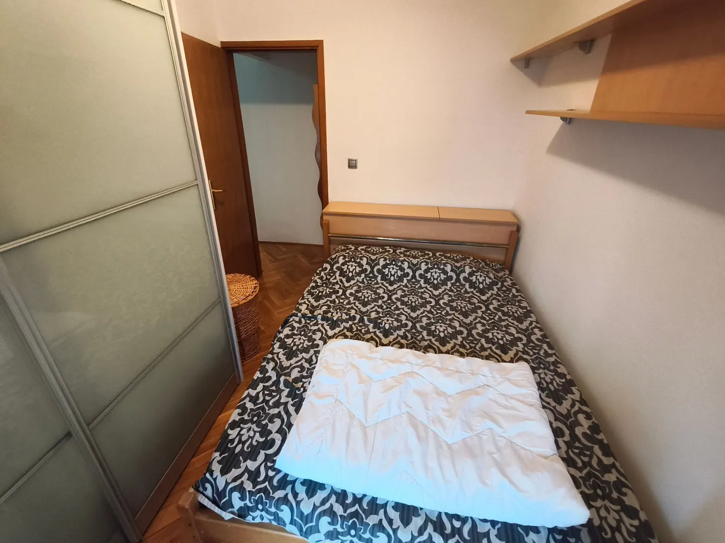 Manja spavaća soba sa krevetom, plakarom i zidnom policom.