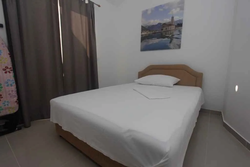 Jednostavna spavaća soba sa bračnim krevetom i slikom na zidu.
