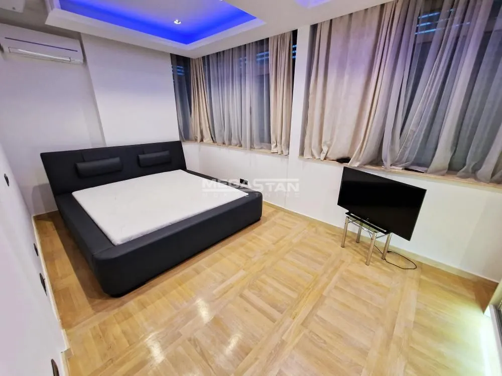 A bedroom with a large double bed, a TV, and hardwood flooring.