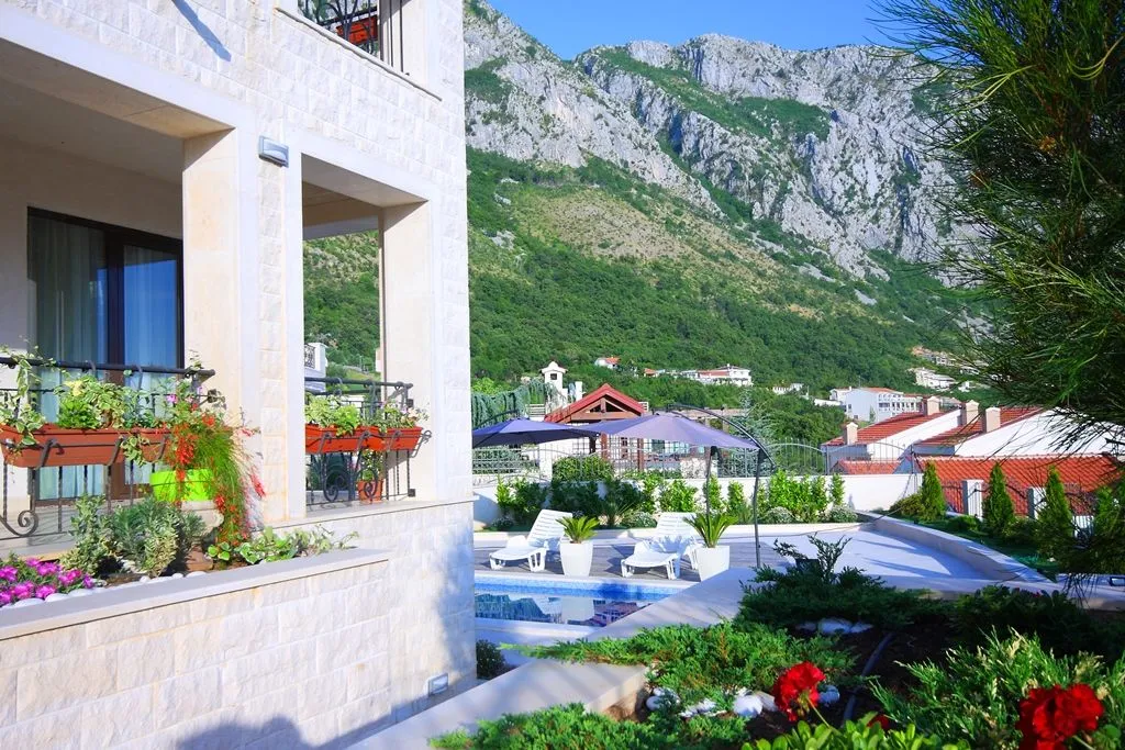Vanjski dio kuće sa bazenom, uređenim dvorištem i pogledom na planinu.
