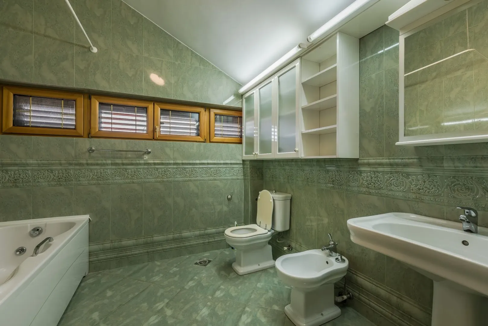 Spacious bathroom with green tiles, a bathtub, and a bidet.