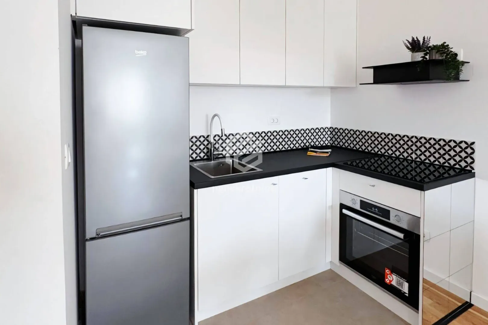 Small modern kitchen with white cabinets, black countertop, and refrigerator.