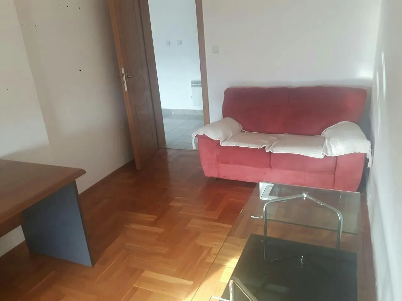 Dnevna soba sa crvenim dvosjedom, staklenim stolom i drvenim podom.