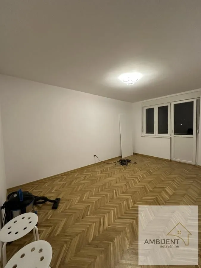 Prazna prostorija sa parketom i belim zidovima.