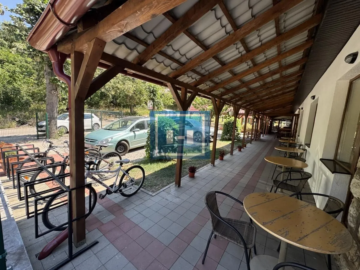 Covered terrace with tables and chairs in front of the building, next to the parking lot and bicycles.