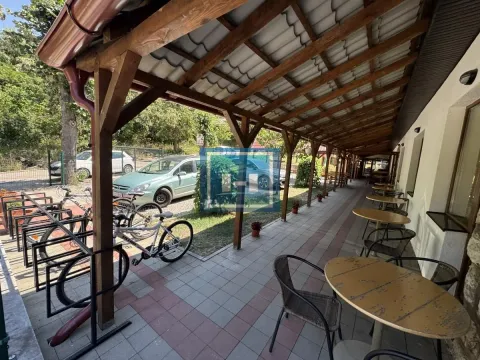 Covered terrace with tables and chairs in front of the building, next to the parking lot and bicycles. - image 22