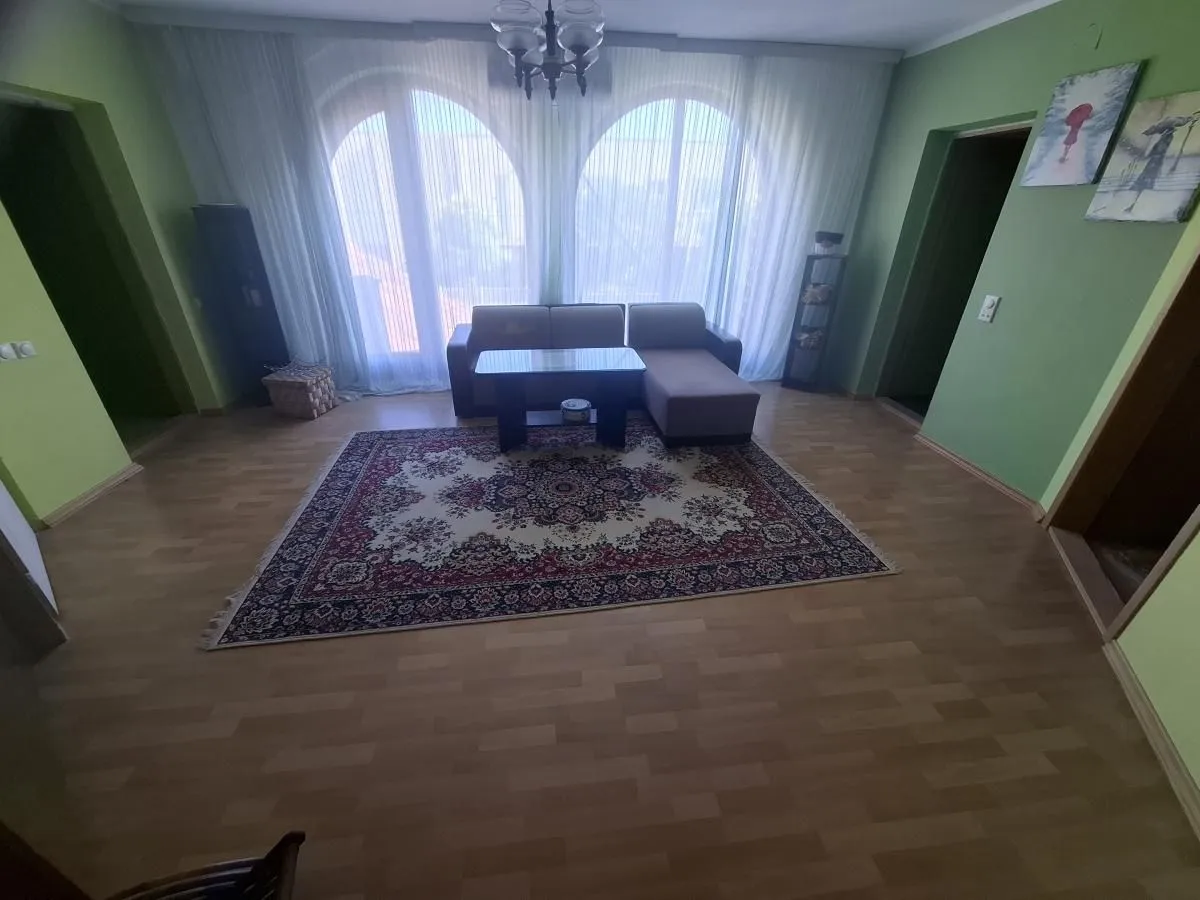 Dnevna soba sa garniturom, tepihom i velikim prozorima.