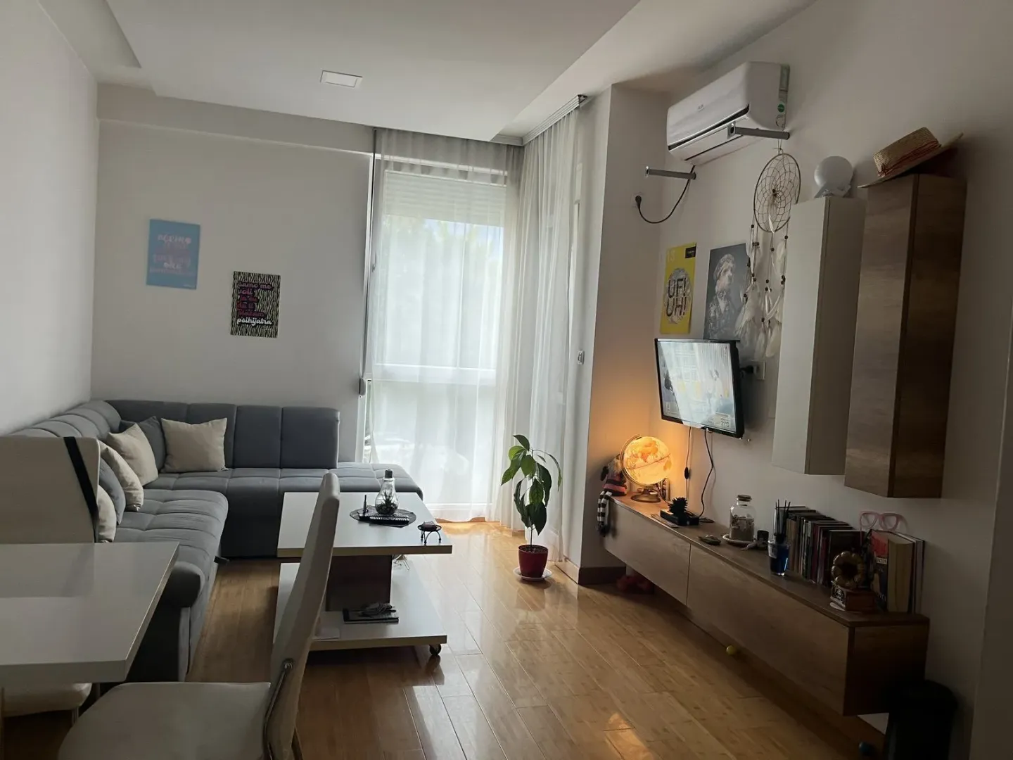 Svijetla dnevna soba sa sivom ugaonom garniturom i drvenim podom.