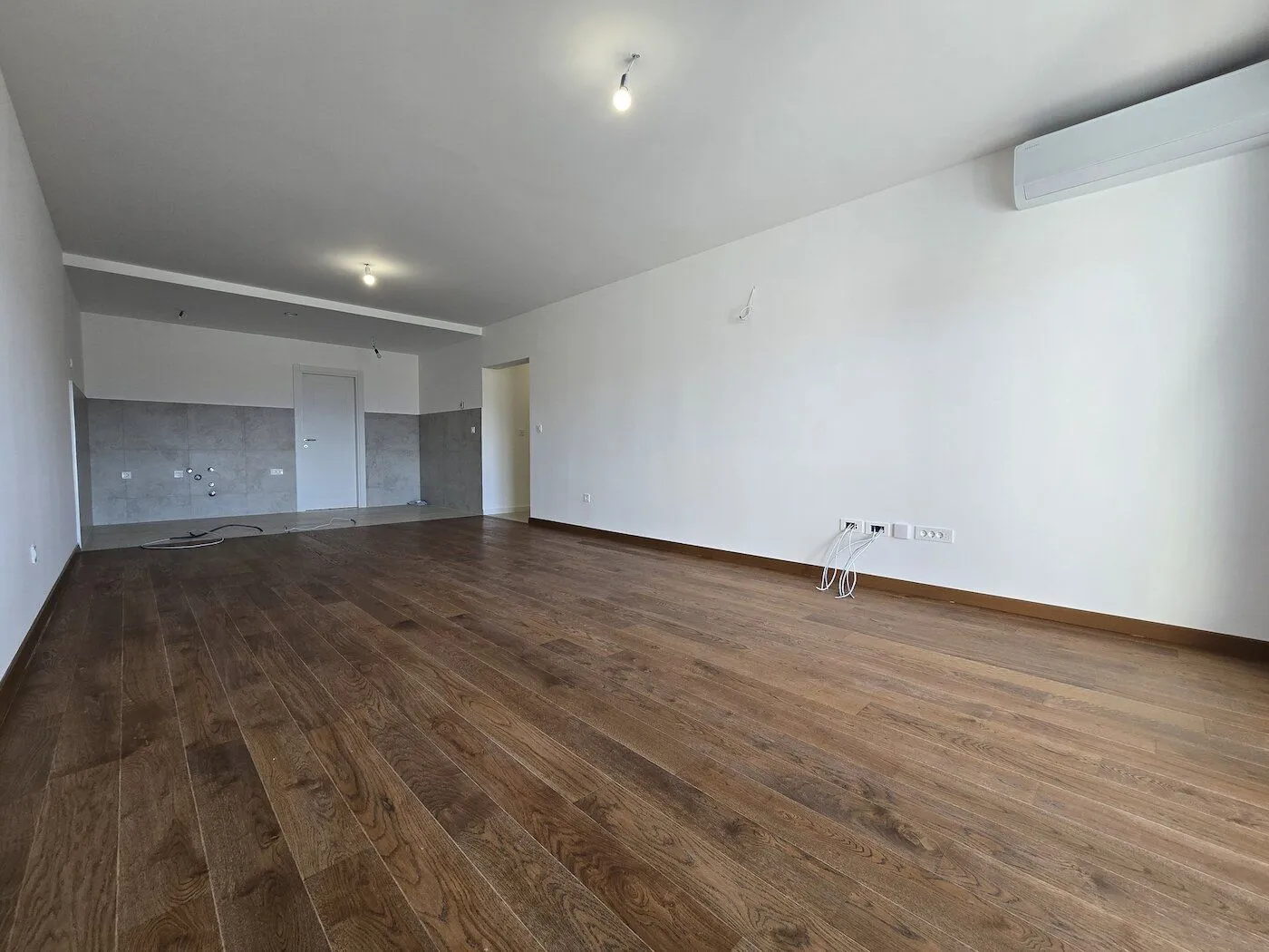 Empty room with wooden flooring and white walls.