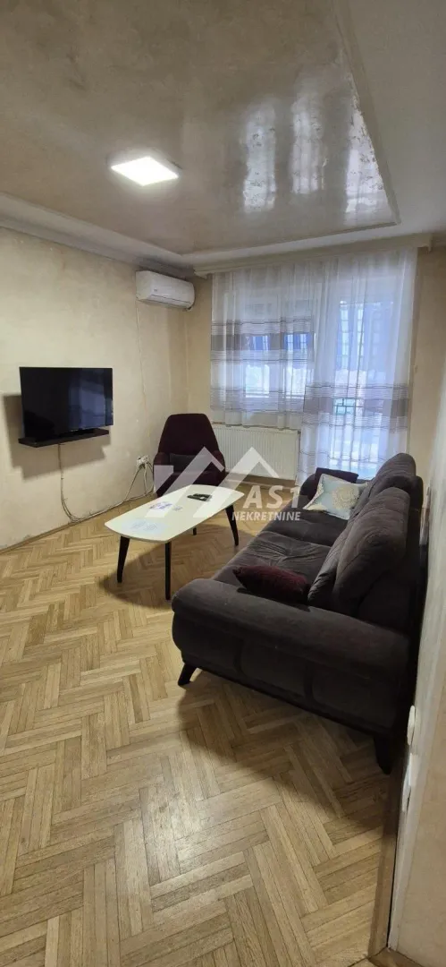 Dnevna soba sa garniturom, stočićem i televizorom na zidu.