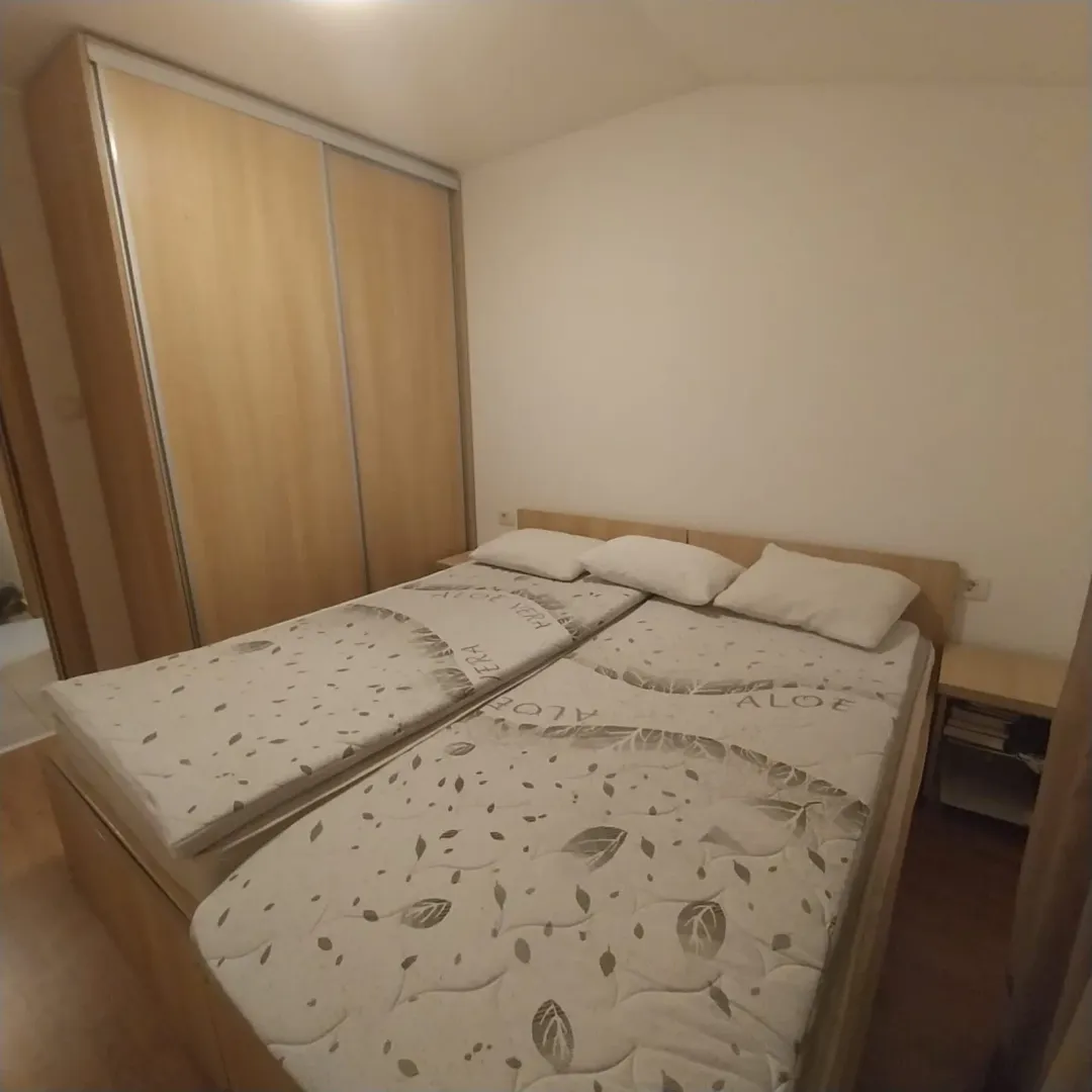 Namještena spavaća soba sa bračnim krevetom i ugradnim plakarom.