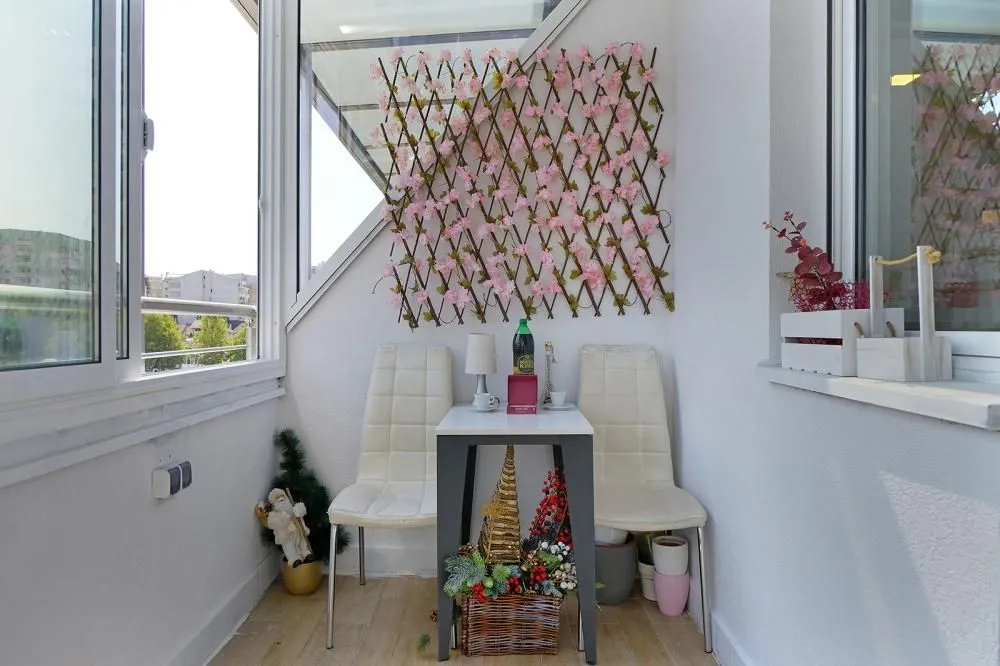 Zastakljeni balkon sa malim stolom, dve stolice i dekorativnim elementima.
