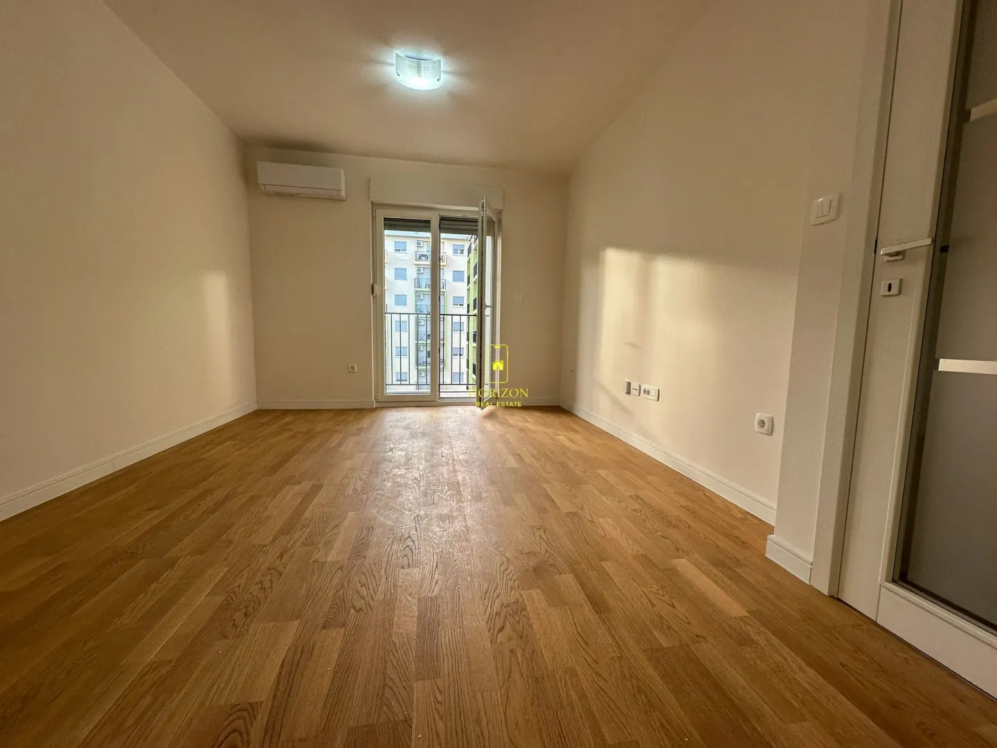 Prazna soba sa drvenim podom i izlazom na balkon.