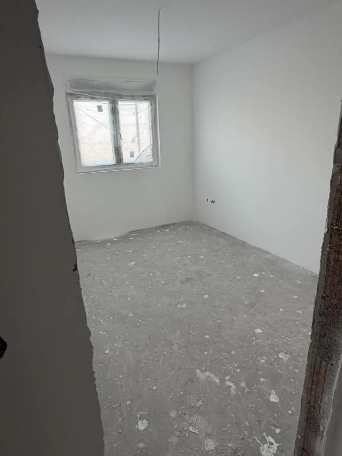 Prazna prostorija u sirovom stanju sa bijelim zidovima i jednim prozorom.