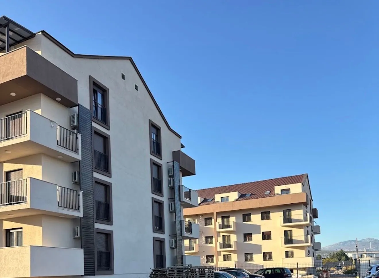 Pogled na spoljašnjost moderne stambene zgrade sa balkonom i parkingom.