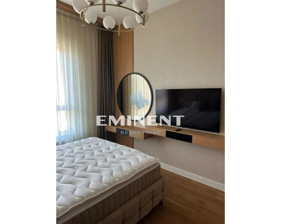 Modern bedroom with a double bed, wall-mounted TV, and a round mirror.