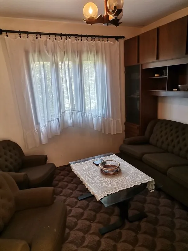Dnevna soba sa garniturom za sedenje, stočićem i prozorom sa belim zavesama.