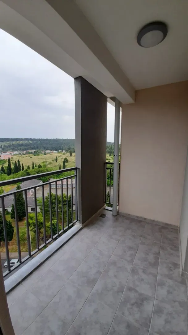 Popločana terasa sa metalnom ogradom i pogledom na prirodu.