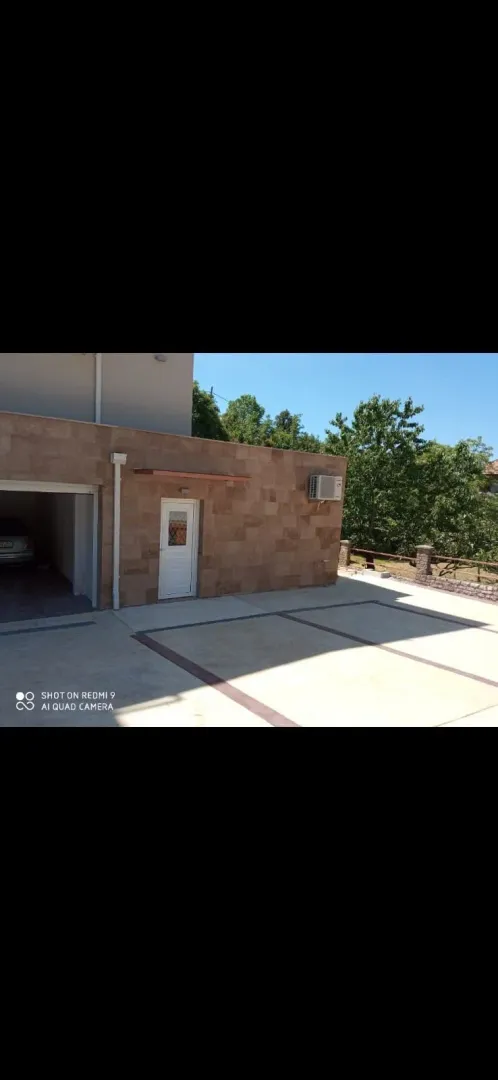 Eksterijer kuće sa popločanim dvorištem i garažom.