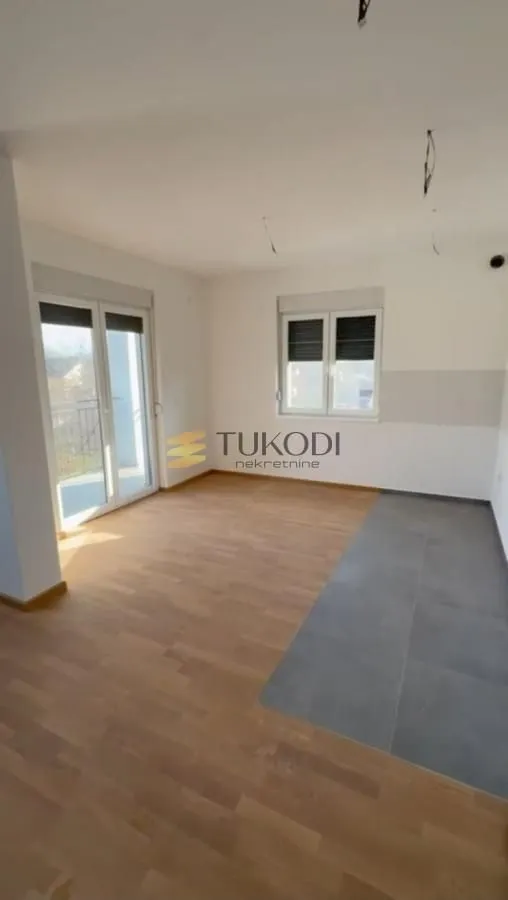 Prazna prostorija sa parketom i keramičkim pločicama na podu, te izlazom na terasu.