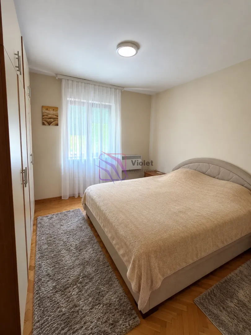 Bedroom with a double bed, built-in wardrobe, and a window with white curtains.
