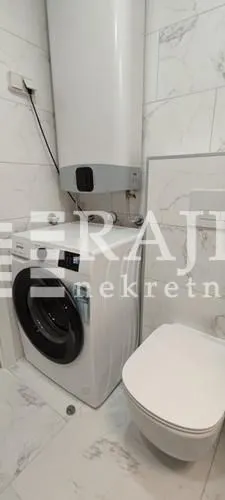 View of the bathroom with a washing machine, water heater, and toilet bowl.