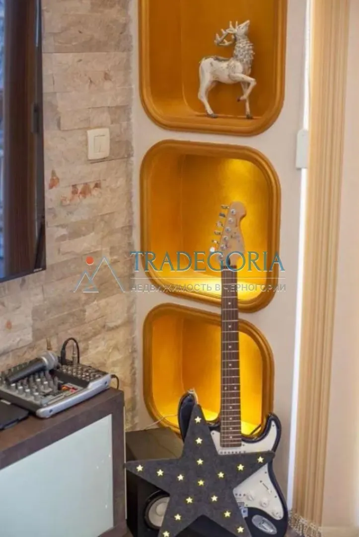 Detalj enterijera sa dekorativnim nišama, gitarom i zvučnom opremom.