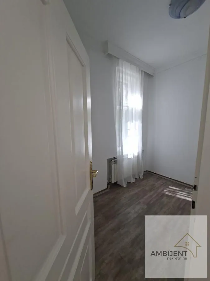 View of an empty room with white walls and a window through an open door.