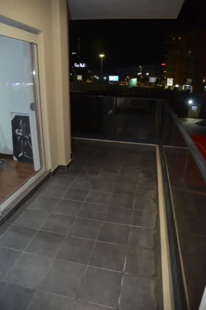 Balcony with dark tiles, a glass railing, and a city view at night.