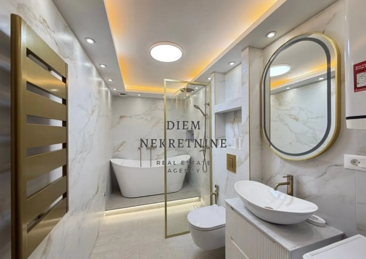 Modernly equipped bathroom with a bathtub, shower cabin, and white marble tiles.
