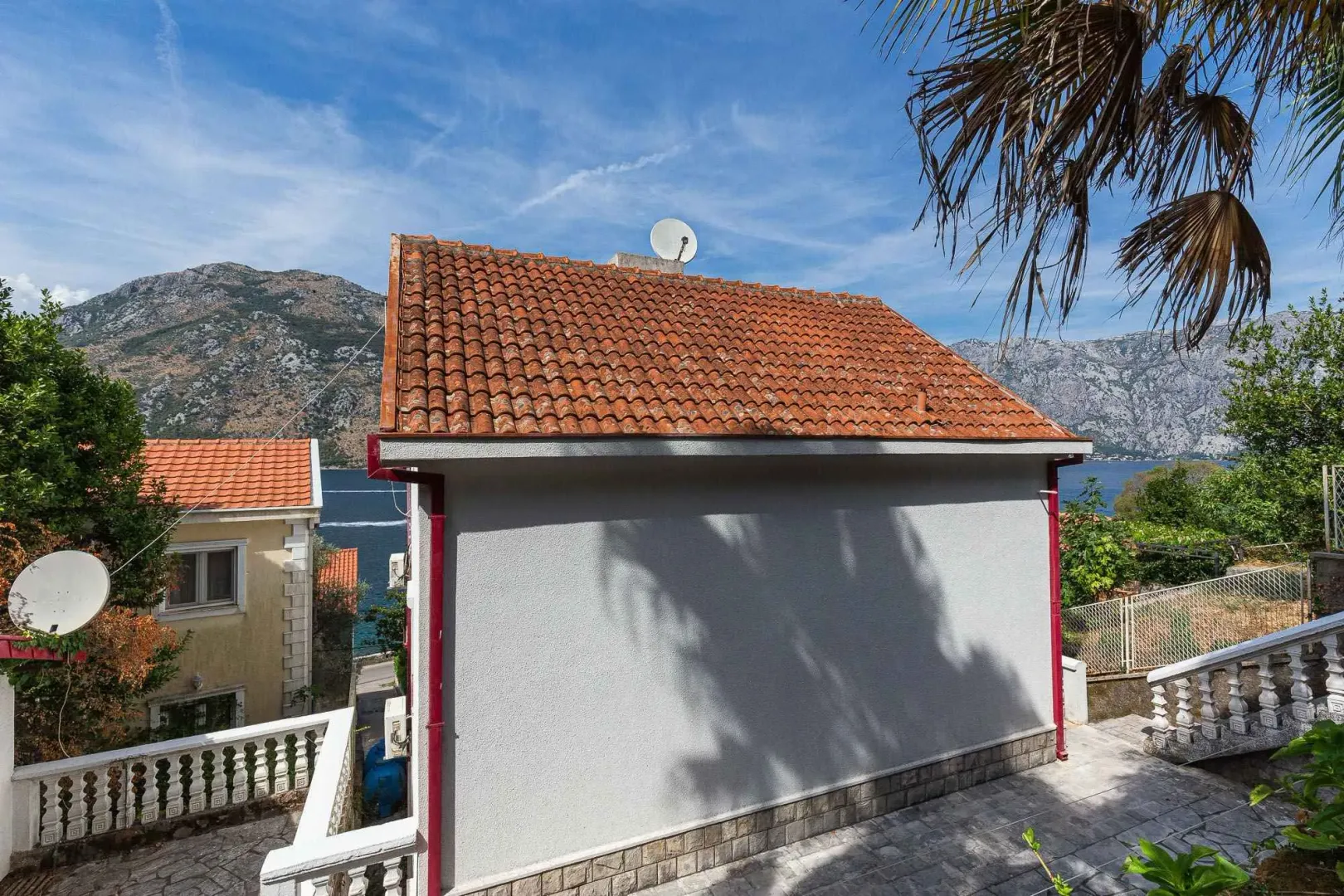 Pogled na spoljašnjost kuće sa popločanim dvorištem i pogledom na more.