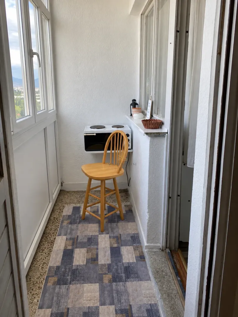 Zastakljeni balkon sa stolicom, malom peći i tepihom.
