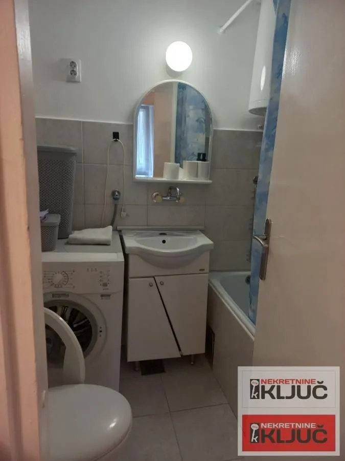 Manje kupatilo sa umivaonikom, kadom, WC šoljom i veš mašinom.
