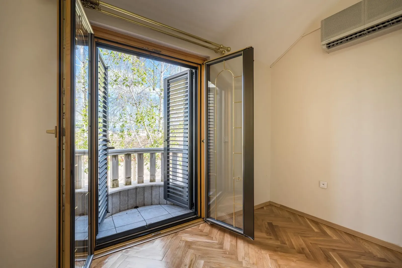 Bright empty room with parquet flooring and open balcony doors.