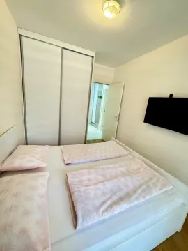Svjetla spavaća soba sa bračnim krevetom, bijelim garderoberom i zidnim televizorom. - image 7