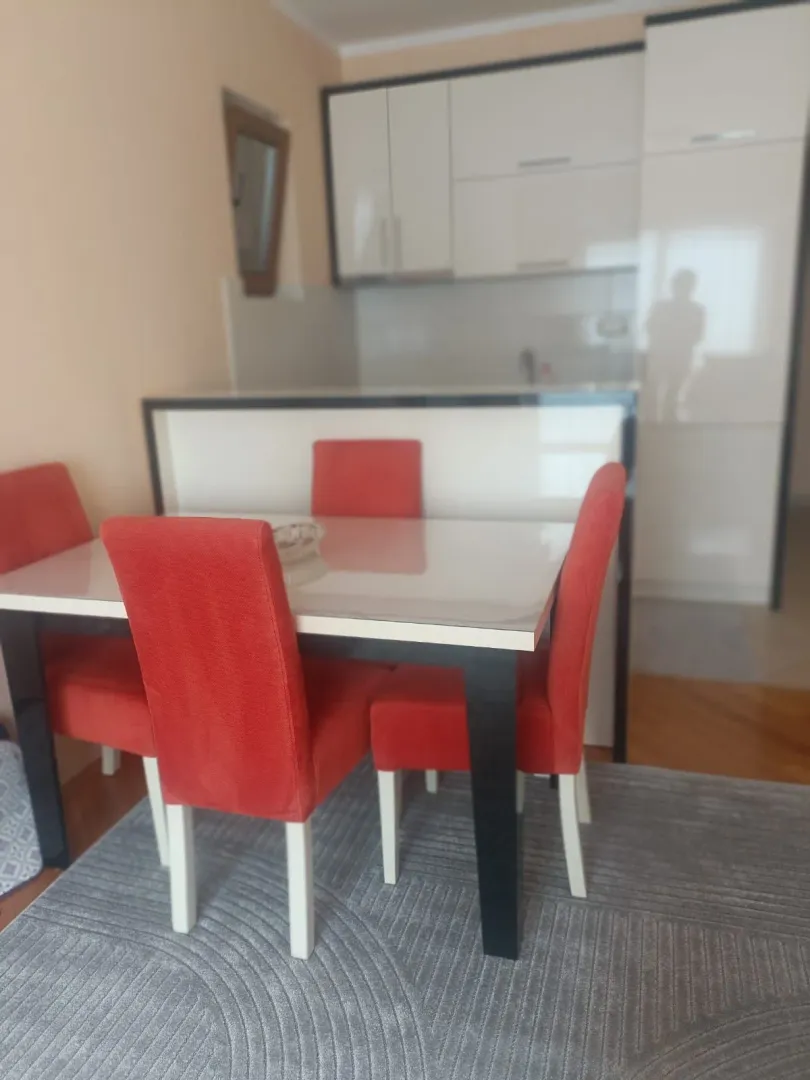 Trpezarija sa crvenim stolicama i kuhinja u pozadini.