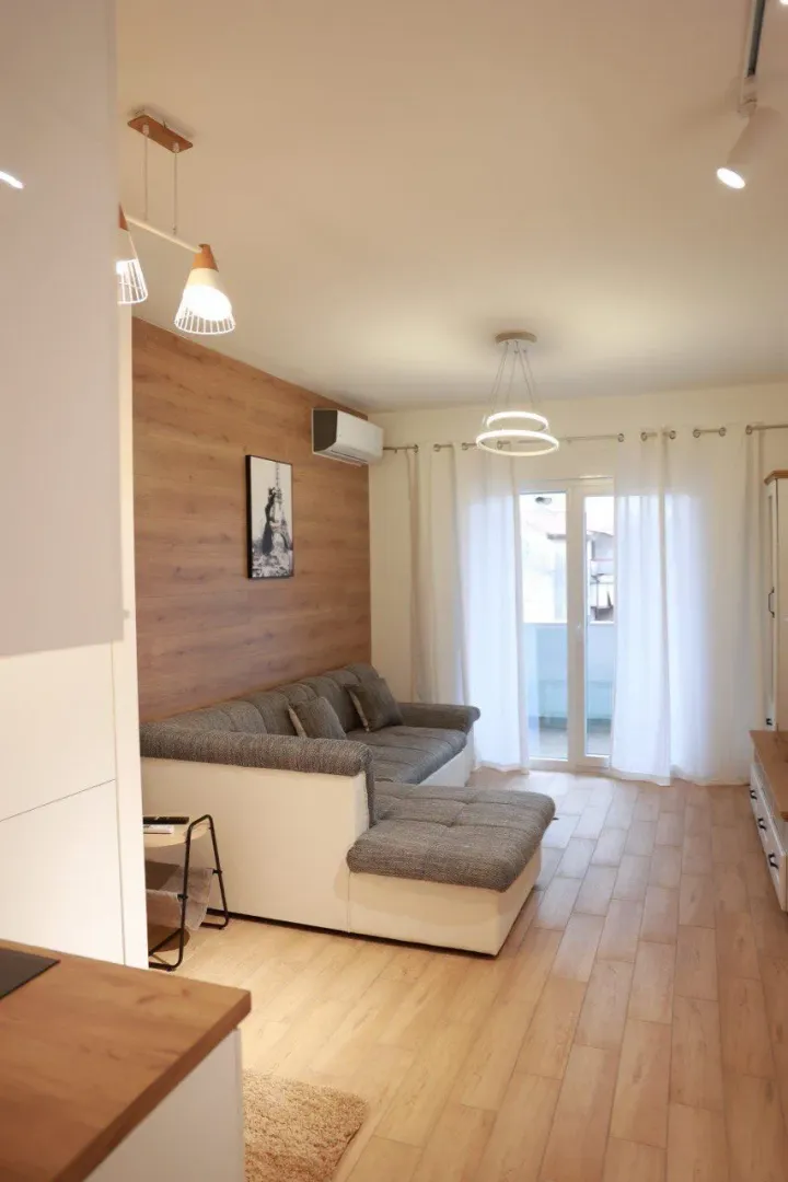 Living room with a corner sofa, wooden wall panel, and access to the terrace.