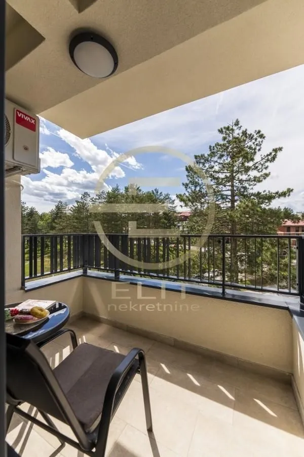 Natkriveni balkon sa garniturom za sjedenje i pogledom na zelenilo.