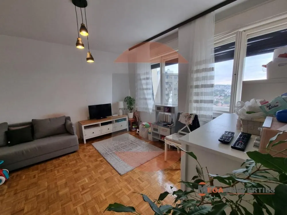 Living room with a sofa, TV unit, and windows overlooking the city.