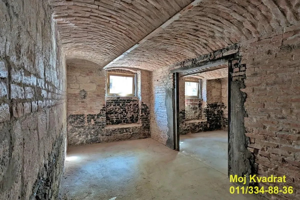 Neuređena prostorija u suterenu sa svodovanim plafonom od cigle i prozorima.