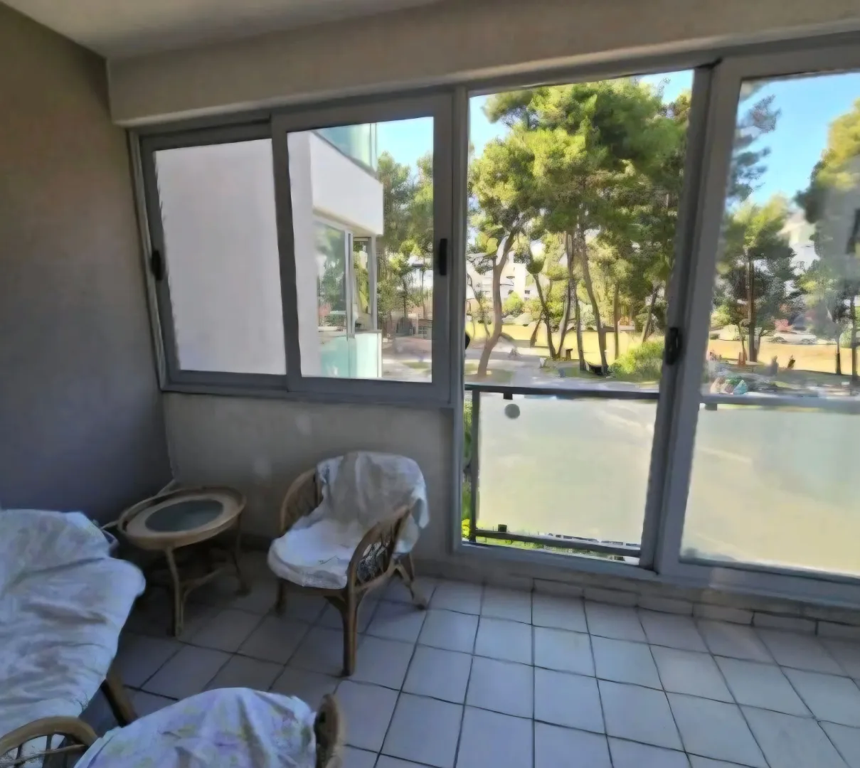 Enclosed balcony with seating furniture and a green view.