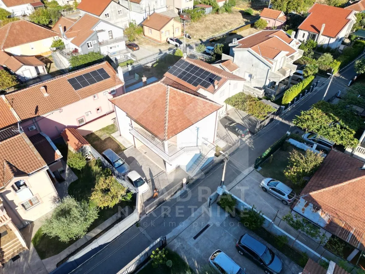 Pogled iz vazduha na kuću i okolno naselje sa solarnim panelima na krovu.